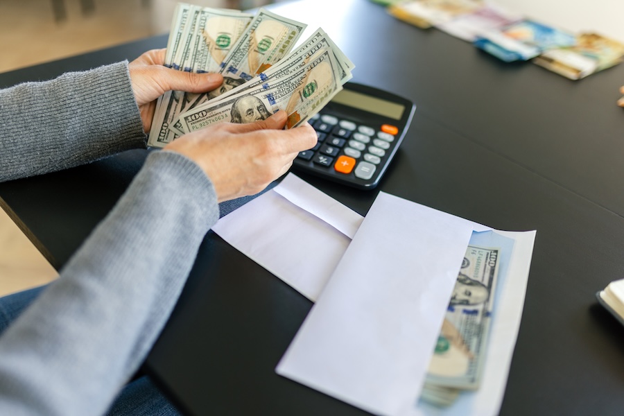 Someone counting hundred-dollar bills next to a calculator and a cash envelope