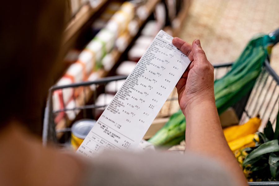 A shopper reading a long grocery receipt beside a full cart