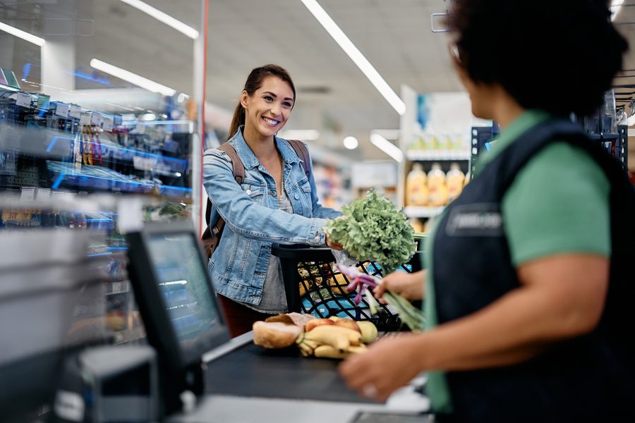 A shopper smiling at a cashier while checking out at a grocery store register