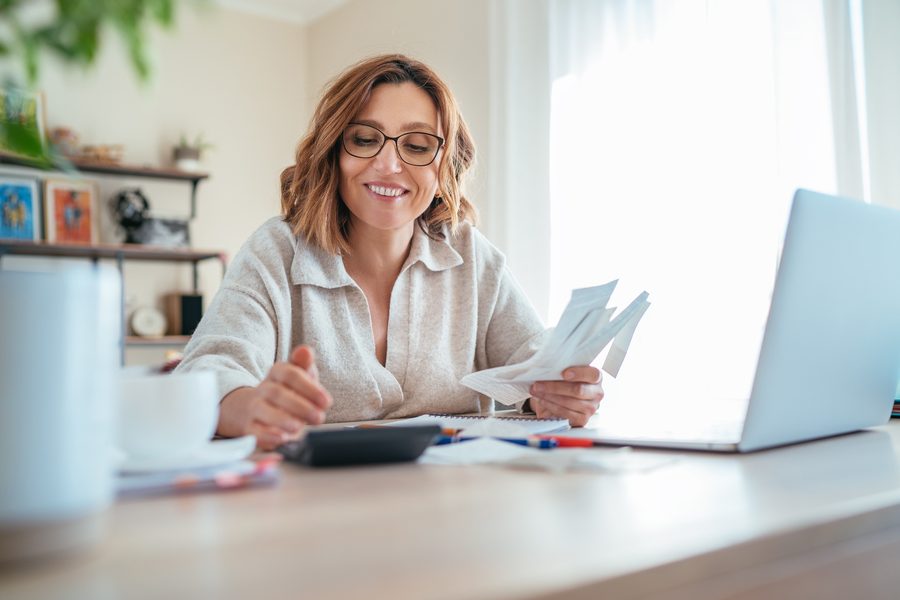 A woman calmly reviewing paperwork and a calculator at her desk at home