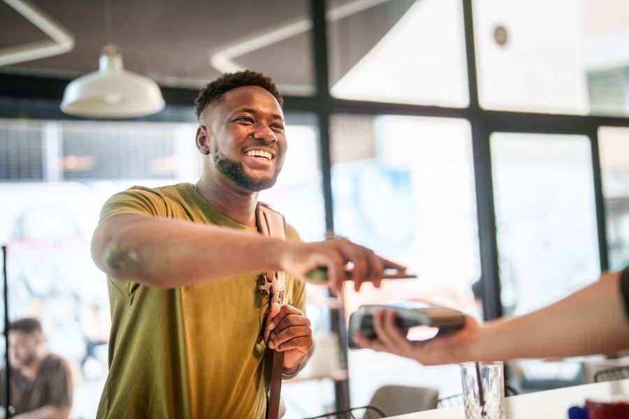 A smiling man tapping his card to pay at a cafe counter