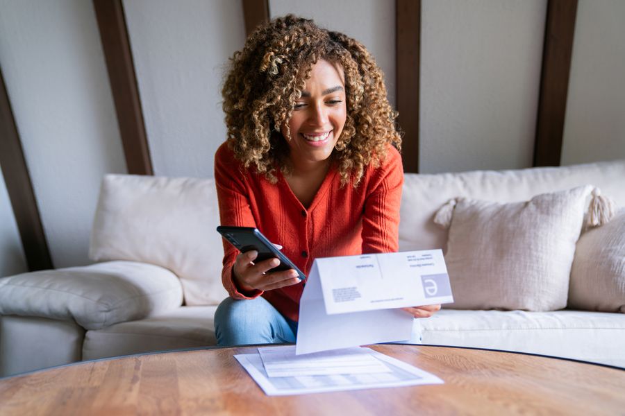 A woman on her couch comparing a paper statement with her banking app