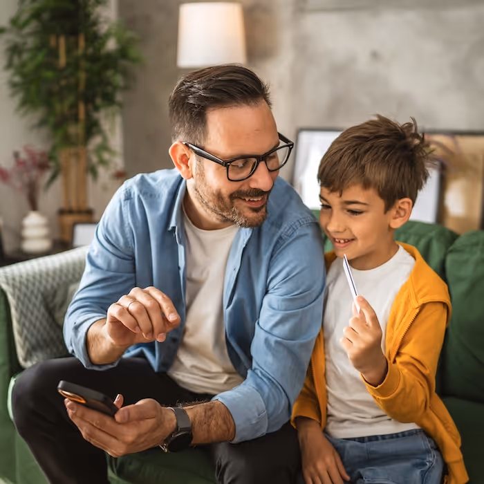 A man and a young boy smiling at a phone together