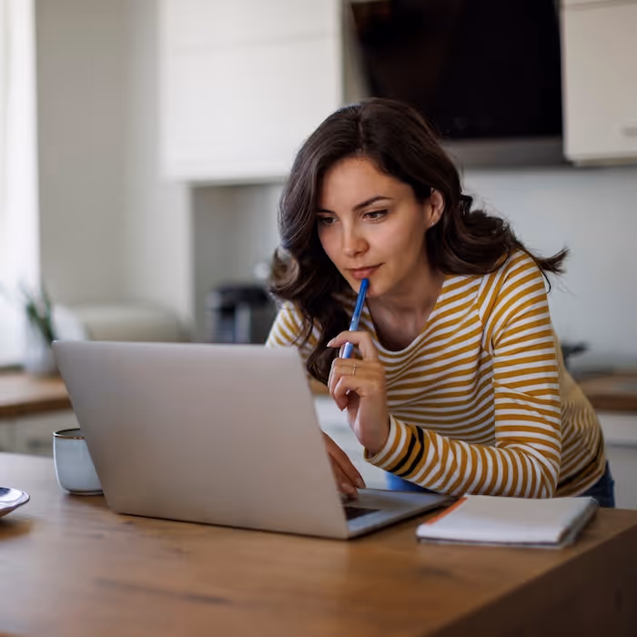 A woman looking thoughtfully at her laptop at the kitchen table